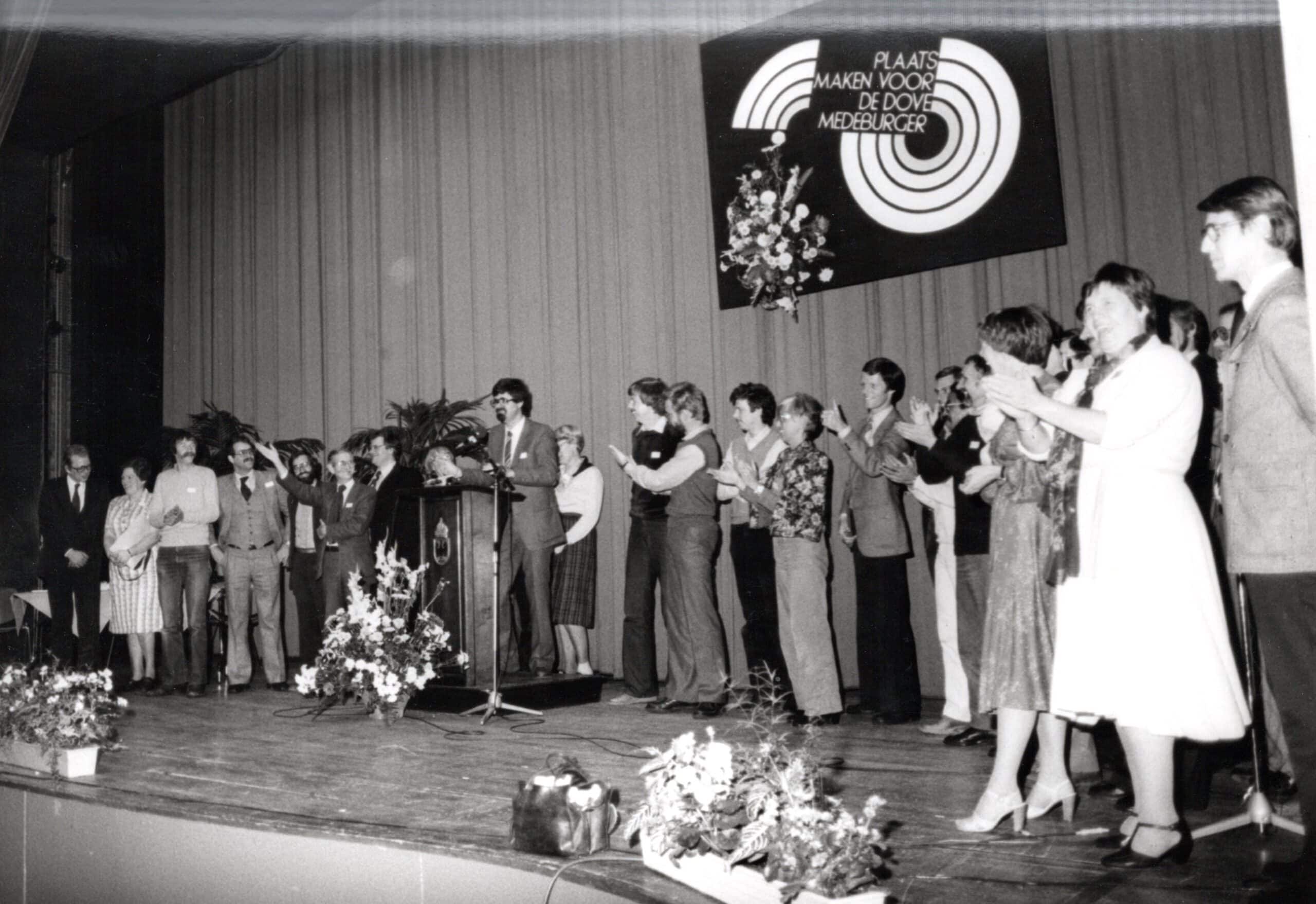 Een groep mensen staat in een halve cirkel op een podium